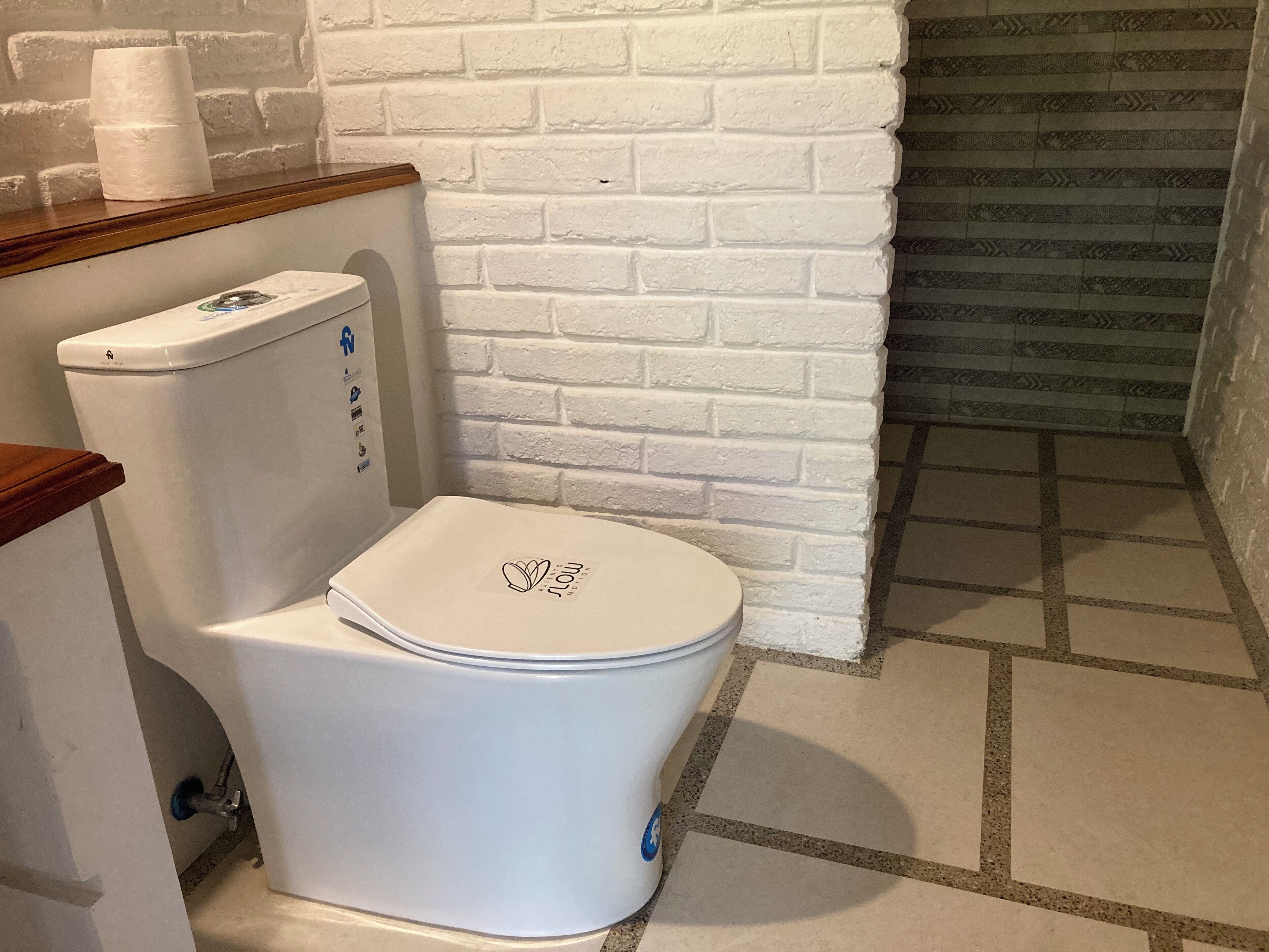 Inodoro blanco con tapa que tiene un logotipo, pared de ladrillo blanco y encimera de madera.