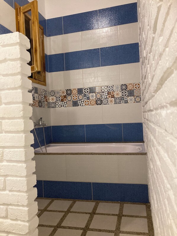 A bathroom with blue and white tiles, a bathtub, and a shower area. - Hotel La Costa International (Salango)