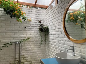 A bathroom with a white brick wall, a round mirror, a sink, and hanging plants. - Hotel La Costa International (Salango)