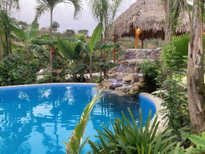 A pool surrounded by tropical vegetation and a small waterfall. - Hotel La Costa International (Salango)