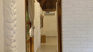 A hallway with white brick walls, wooden beams, and a window with a curtain. - Hotel La Costa International (Salango)