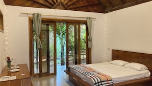 A bedroom with a wooden ceiling, a bed with white bedding, a wooden desk, and a view through a glass door to an outdoor area with greenery. - Hotel La Costa International (Salango)