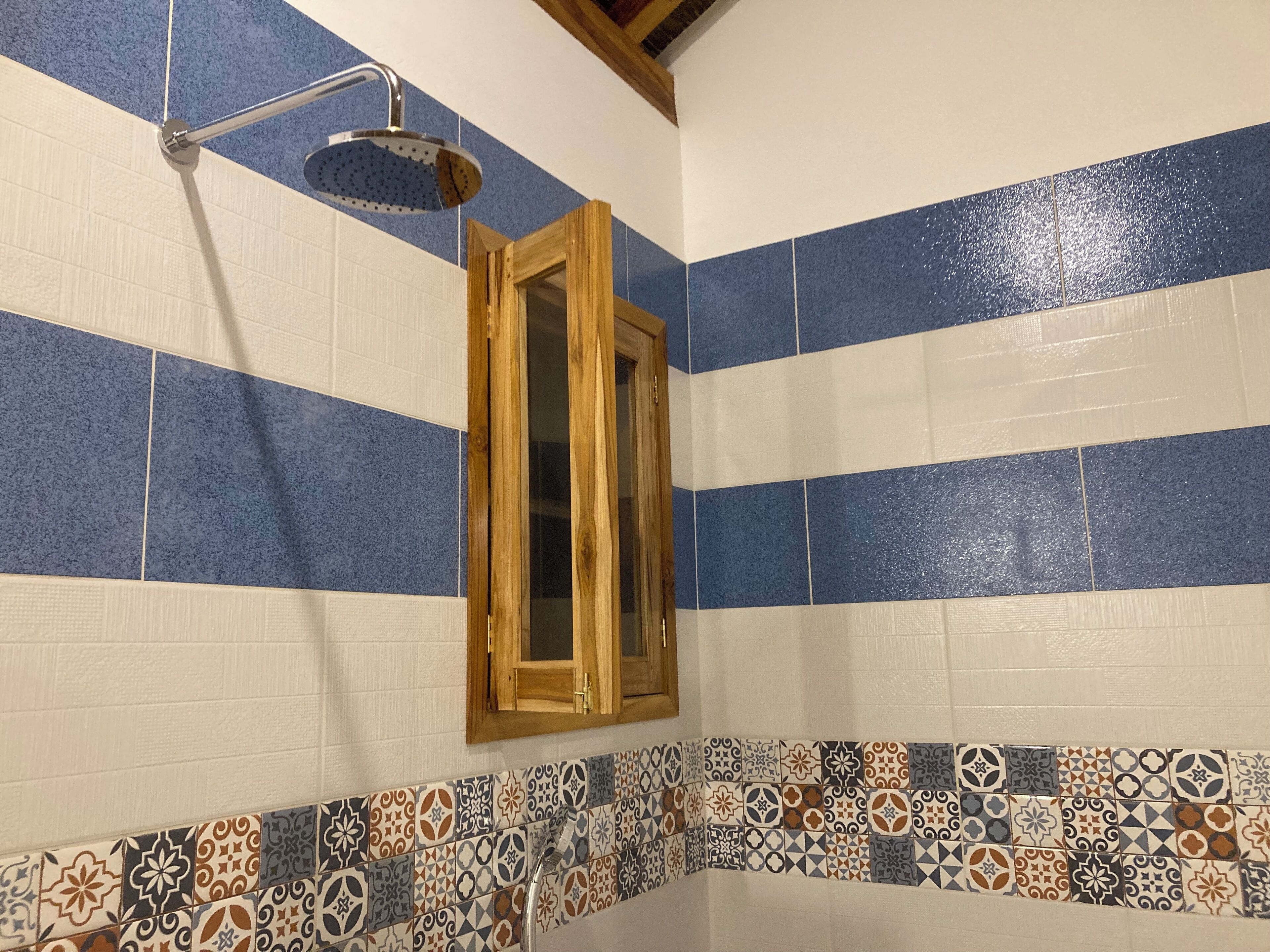 A bathroom with blue and white striped tiles, a showerhead, a wooden-framed mirror, and a decorative tile border.