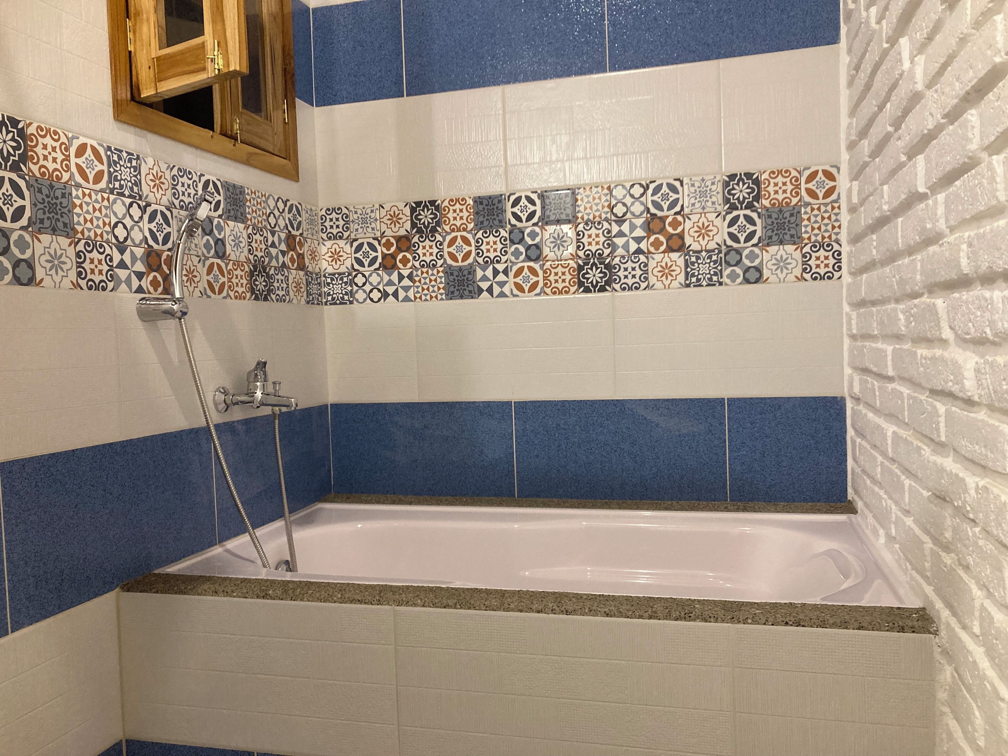 A bathroom with a bathtub, blue and white tiles, a shower, and a wooden cabinet.