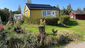 A yellow house with a black roof, surrounded by a well-maintained garden with various plants and a rooster decoration. - 4 Star Holiday Home in Vingaker (Vingåker)