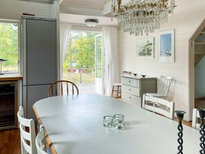 A kitchen with a dining table, chairs, a refrigerator, a chandelier, and a view through the window. - 4 Star Holiday Home in Vaxholm (Vaxholm)
