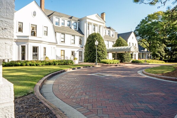 A large, white building with a symmetrical facade, a brick pathway, and well-maintained lawns.