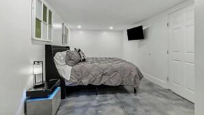 Un dormitorio con cama, televisor montado en la pared y una puerta.