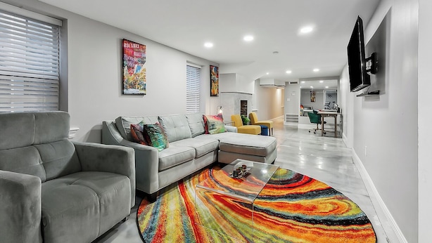 Una sala de estar moderna con un sofá seccional gris, alfombra colorida y obras de arte en las paredes.