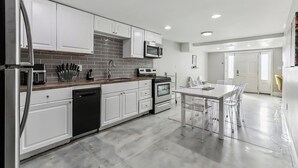 Una cocina moderna con muebles blancos, microondas integrado y comedor con mesa y sillas de vidrio.