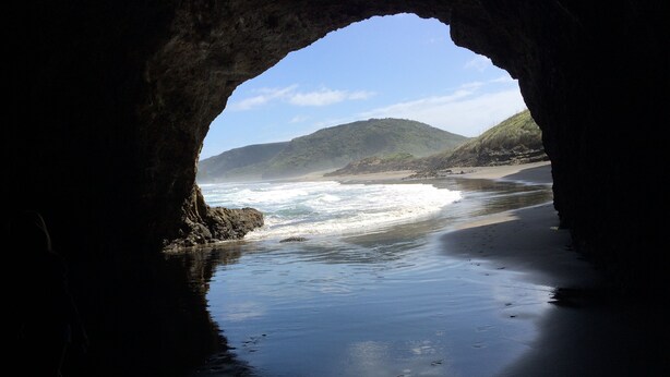 Vistes a una platja a través d'una arcada natural, amb onades que quebres a la riba.