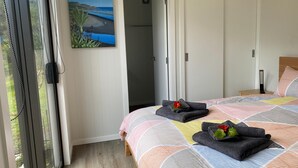 Un dormitori amb un llit, un quadre d'una platja i una vista per una porta oberta.
