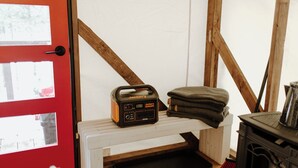 A cozy room with a red door, a Jackery portable power station, a stack of folded blankets, and a wood-burning stove. - Two Queen Beds - All Good in the Woods! (Beaver Bay)
