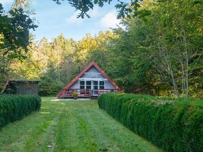 A cabin with a red roof, surrounded by dense greenery and a clear sky.