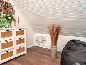 A room with a sloped ceiling, a white dresser with woven baskets, a vase with dried plants, and a black bean bag. - 4 Person Holiday Home in Toftlund (Toftlund)