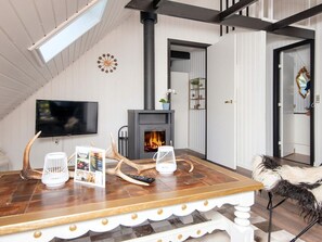 A cozy living room with a fireplace, a television mounted on the wall, and a dining table with a picture frame and a remote control. - 4 Person Holiday Home in Toftlund (Toftlund)