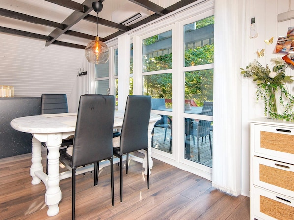 A dining area with a white table and chairs, a hanging light fixture, and a view through large windows. - 4 Person Holiday Home in Toftlund (Toftlund)