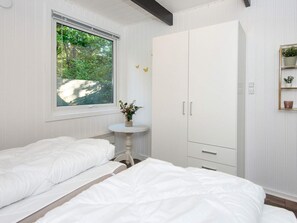 A bedroom with two beds, a window with a view of greenery, a white wardrobe with drawers, and a small table with a vase. - 4 Person Holiday Home in Toftlund (Toftlund)