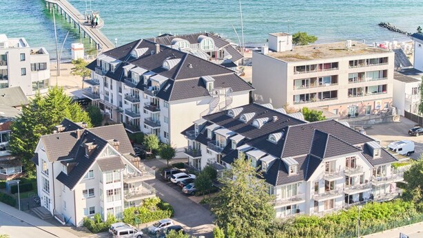 A coastal residential area with modern apartment buildings, a pier extending into the sea, and a parking area with cars. - Residence Johannsens B 12 - Residence Johannsens (Timmendorfer Strand)