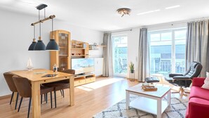 A modern living room with a wooden dining table, a flat-screen TV, and a red sofa. - Residence Johannsens B 12 - Residence Johannsens (Timmendorfer Strand)