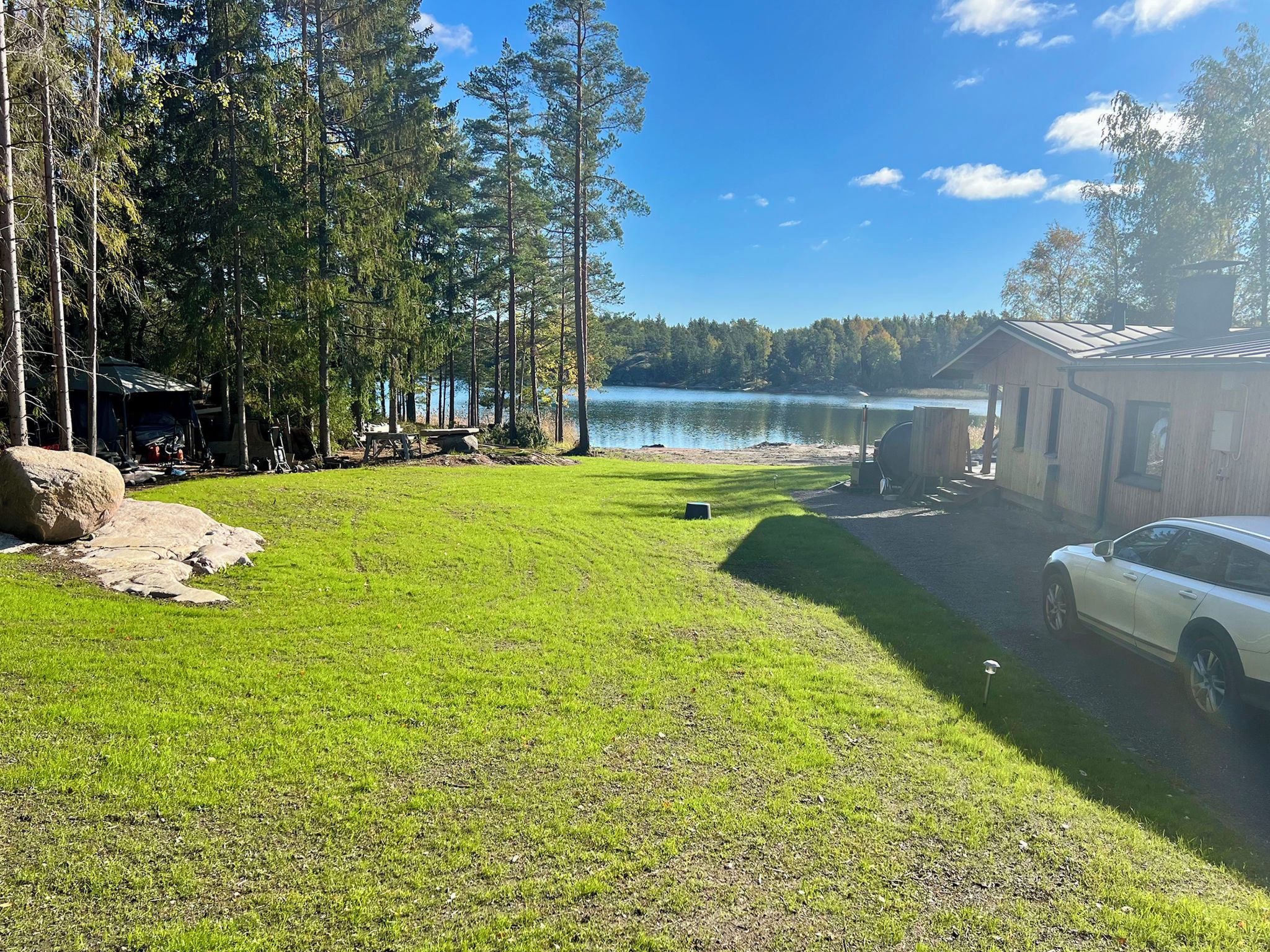 Eine Ferienhütte am See mit Rasen, einem Steg und einem geparkten Auto in der Nähe.