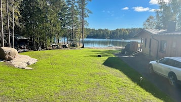 Eine Ferienhütte am See mit Rasen, einem Steg und einem geparkten Auto in der Nähe.