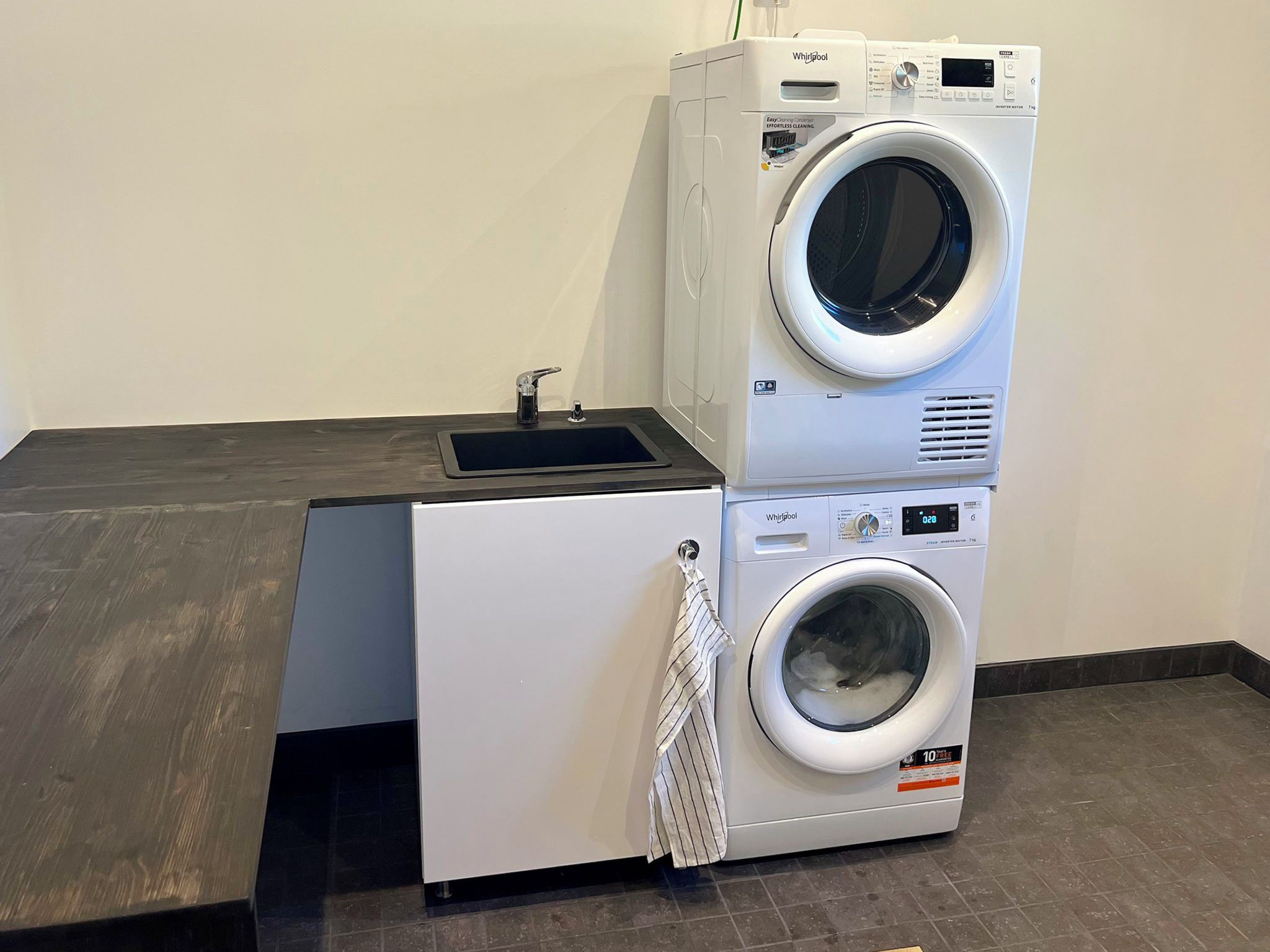 Un espace buanderie compact comprenant deux machines à laver superposées et un petit évier.