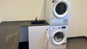 Un espace buanderie compact comprenant deux machines à laver superposées et un petit évier.