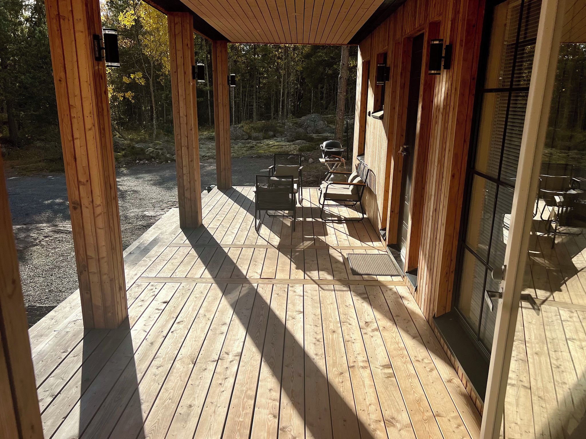 A wooden deck with outdoor seating and a glass door leading to a covered area.