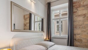 Une chambre à coucher avec un lit, un grand miroir, une lampe et une vue sur un mur en pierre et une fenêtre.