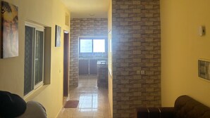 Un couloir doté d’un sol carrelé, d’un mur en pierre et d’une fenêtre au fond, donnant sur un espace cuisine.