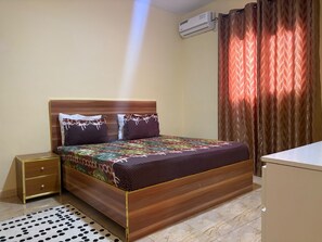 Une chambre à coucher bien rangée, avec un lit en bois, une table de chevet, une commode et un tapis à motifs.