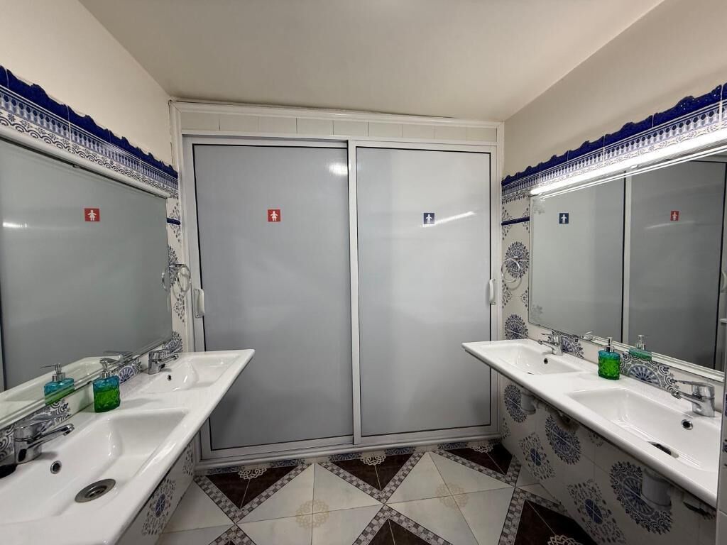 A bathroom with two sinks, a mirror, and a door with a red emergency exit sign.