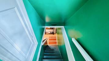 A staircase with teal walls and white trim, leading to a room with a bed and a nightstand.
