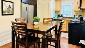 A kitchen with wooden cabinets, a dining table with chairs, a coffee maker, and a stove. - Campu's Whole House (Cherry Hill)