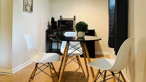 A compact kitchen with a microwave, coffee machine, and a small potted plant on the counter. There are two white chairs around a round table. - Campu's Whole House (Cherry Hill)