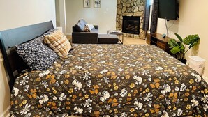 A bedroom with a large bed, a sofa, a fireplace, and a TV. - Campu's Whole House (Cherry Hill)