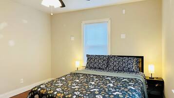 A bedroom with a bed, a ceiling fan, a window with blinds, and two bedside lamps.
