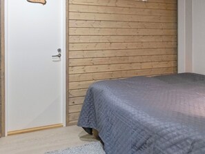 A bedroom with a wooden wall, a bed with a grey quilt, and a white door. - Villa uuttu by Interhome (Pelkosenniemi)