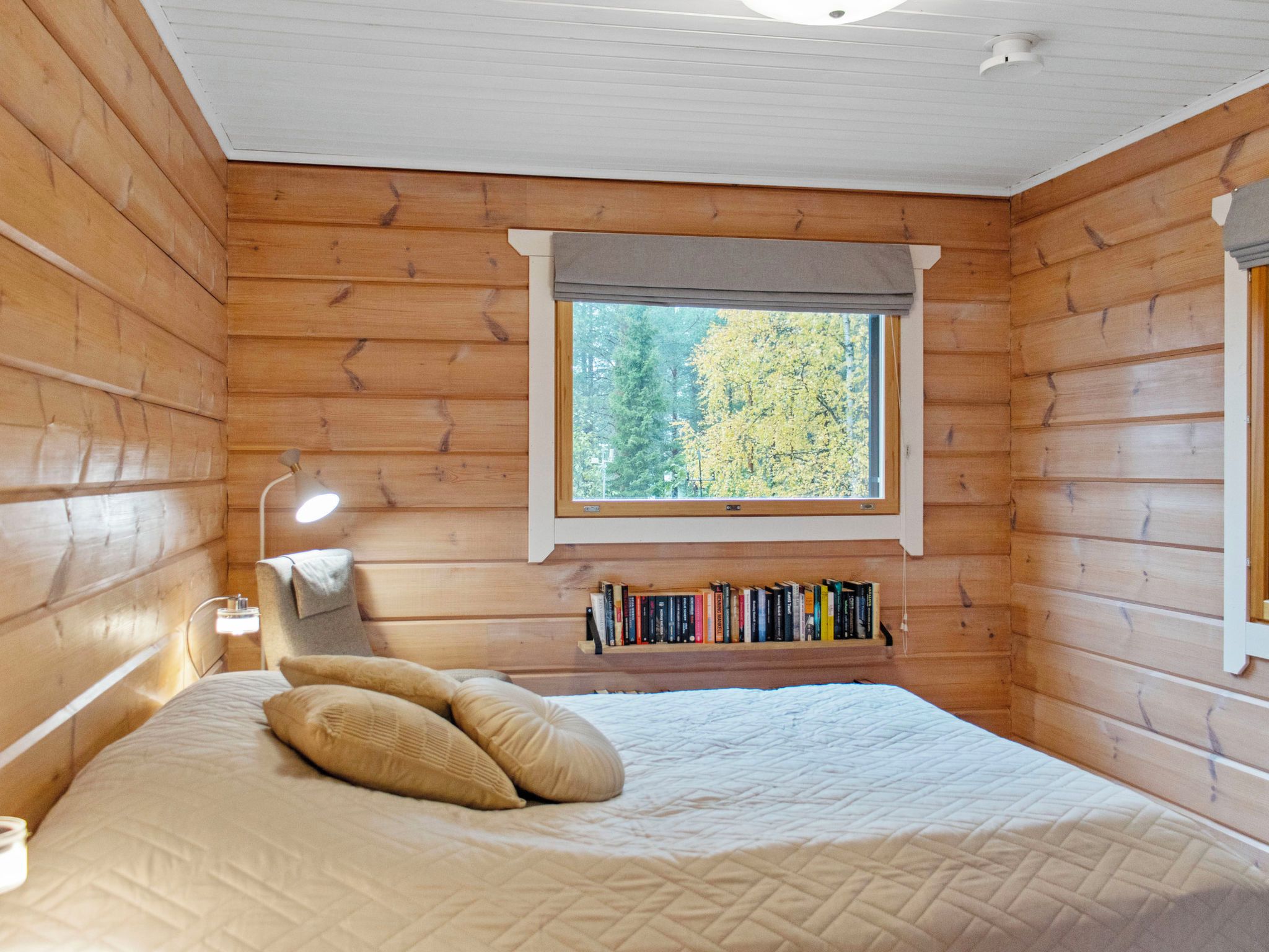 Une chambre à coucher dans un chalet en bois, avec un lit, des oreillers, une lampe de chevet, une fenêtre et une bibliothèque.