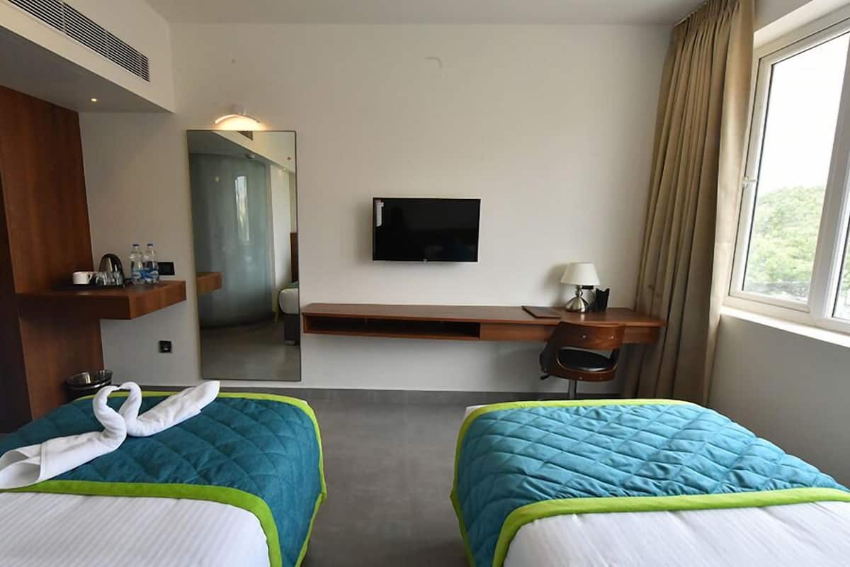 A hotel room with two beds, a TV, a desk, and a window.