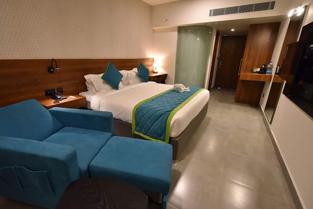 A hotel room with a bed, a blue sofa, a nightstand with a phone, and a wall-mounted lamp.