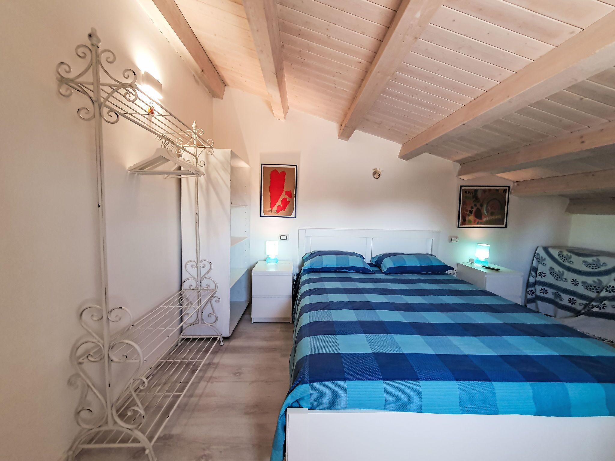 Een slaapkamer met een bed, een nachtkastje, een wandplank en een plafondventilator.