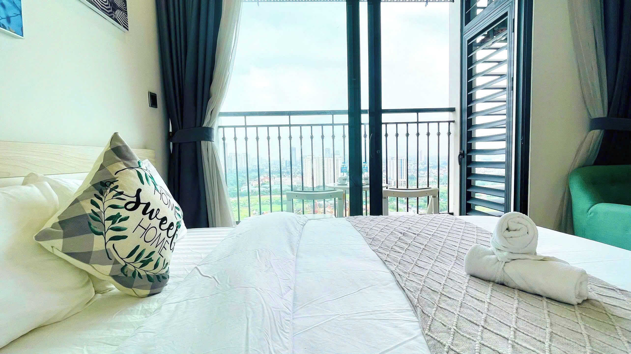 A hotel room with a large bed, a view of the city through the balcony, and a green chair.