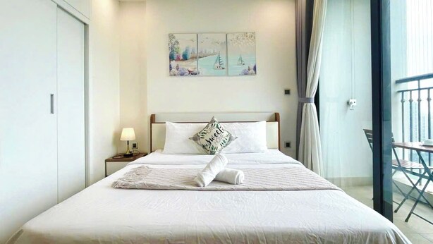 Een net opgemaakt bed met een kussen, een bedlampje en een schilderij erboven.