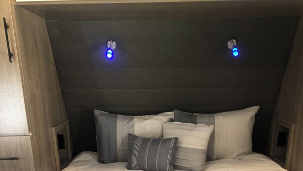 Een slaapkamer met een bed, kussens en een hoofdeinde met ingebouwde verlichting.