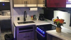 Een compacte keuken met houten kastjes, een ingebouwde oven, een spoelbak en een flatscreen-televisie met een TCL Roku TV interface.
