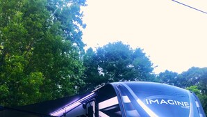 Een caravan met de tekst 'IMAGINE' op de zijkant, geparkeerd op gras met een picknickgedeelte in de buurt.