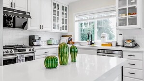 Une cuisine moderne avec des meubles blancs, une cuisinière en acier inoxydable et une grande fenêtre qui laisse entrer la lumière naturelle.