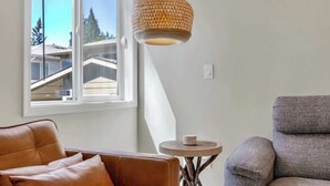 Une pièce dotée d’une grande fenêtre, d’un canapé en cuir marron, d’un fauteuil gris et d’un luminaire suspendu en fibres tressées.
